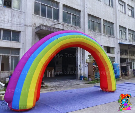 A large inflatable rainbow arch with colorful stripes, set against an industrial backdrop, designed for use as party or event decor.