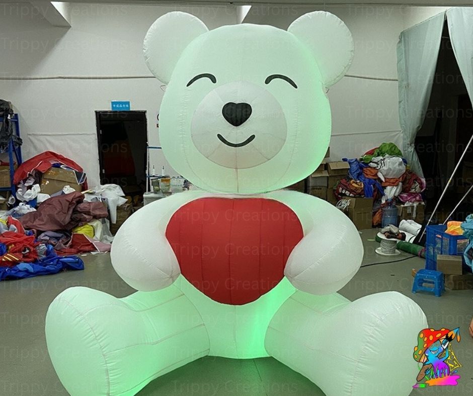 Inflatable teddy bear with a red heart and glowing green base in an indoor setting.
