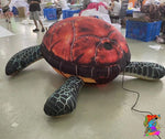 Inflatable sea turtle on a floor with people and blue crates in the background