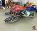 Large inflatable turtle on a concrete floor with boxes and bags in the background