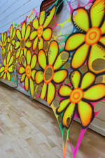Colorful flower-shaped wall art on a wooden floor with a white wall background. Psychedelic backdrops