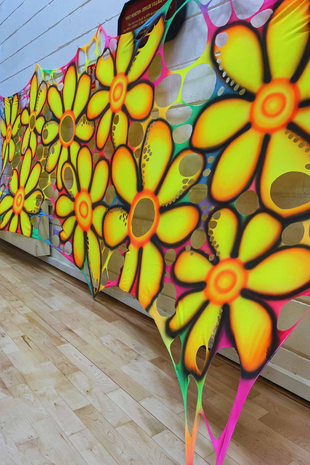 Colorful flower-shaped wall art on a wooden floor with a white wall background. Psychedelic backdrops