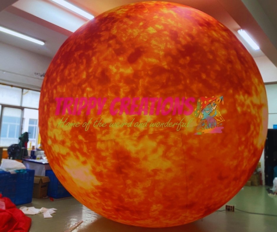 Large inflatable sphere with fiery design and 'Trippy Creations' branding inside a room.