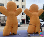 Two large inflatable gingerbread men on a blue tarp outdoors with buildings in the background.