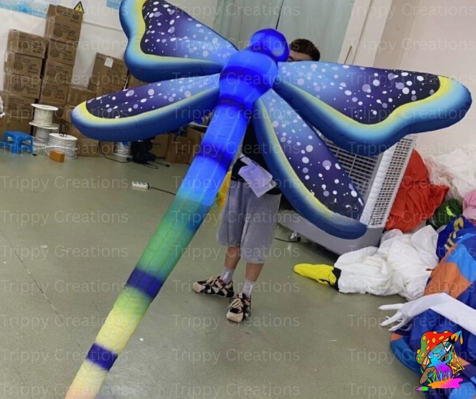 Inflatable dragonfly decoration in a warehouse setting with 'Trippy Creations' branding.