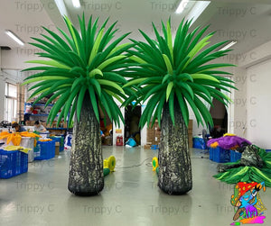 Two large inflatable palm trees in a room with various items and people in the background.