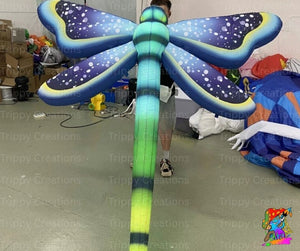 Inflatable dragonfly decoration in a warehouse setting with 'Trippy Creations' branding.