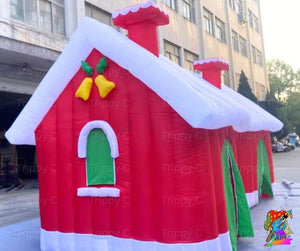 Inflatable Christmas-themed house with red roof, white trim, and green door in an urban setting.