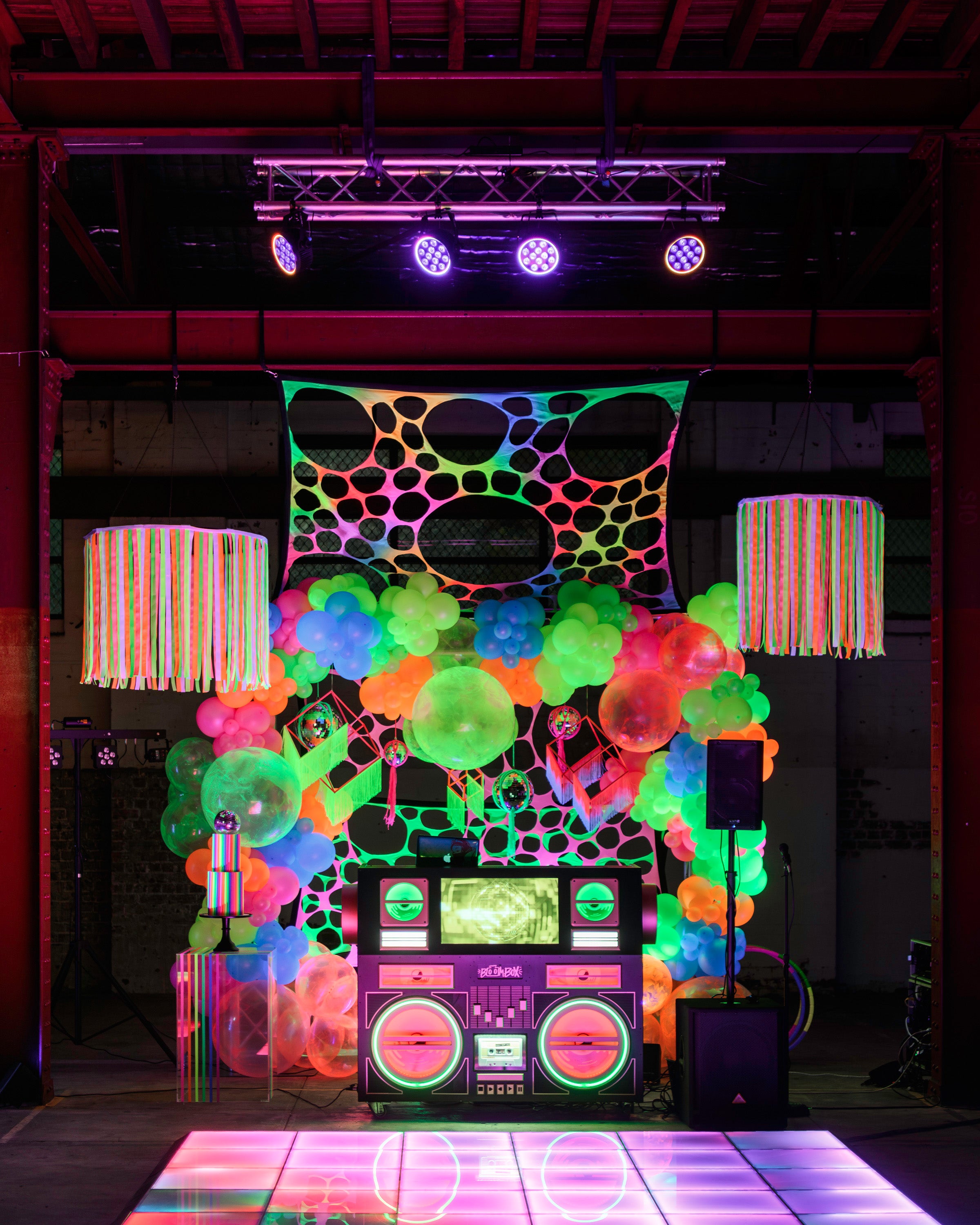 Colorful disco setup with balloons, lights, and a boombox in a dark room.