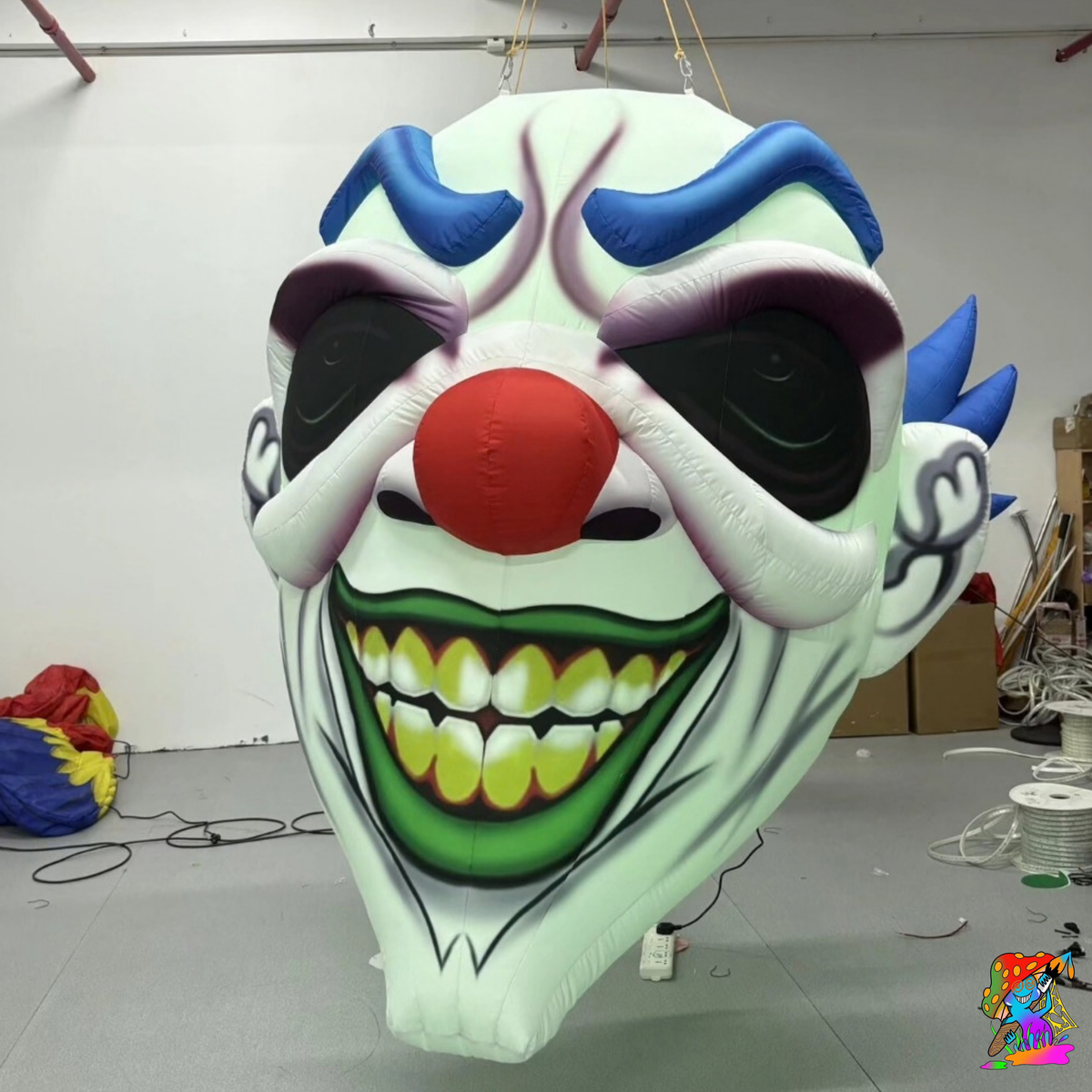 Front view of the handcrafted inflatable Halloween clown head with blue eyebrows, red nose and pointed teeth.
