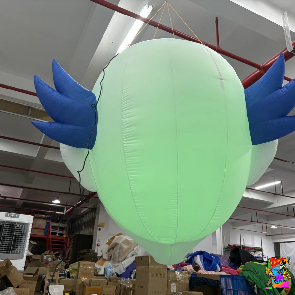 Rear view of the suspended inflatable clown head glowing green, with shaped blue hair on either side.