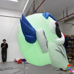 Side and rear view of the green-lit inflatable clown head showing its rounded fabric body and blue hair.