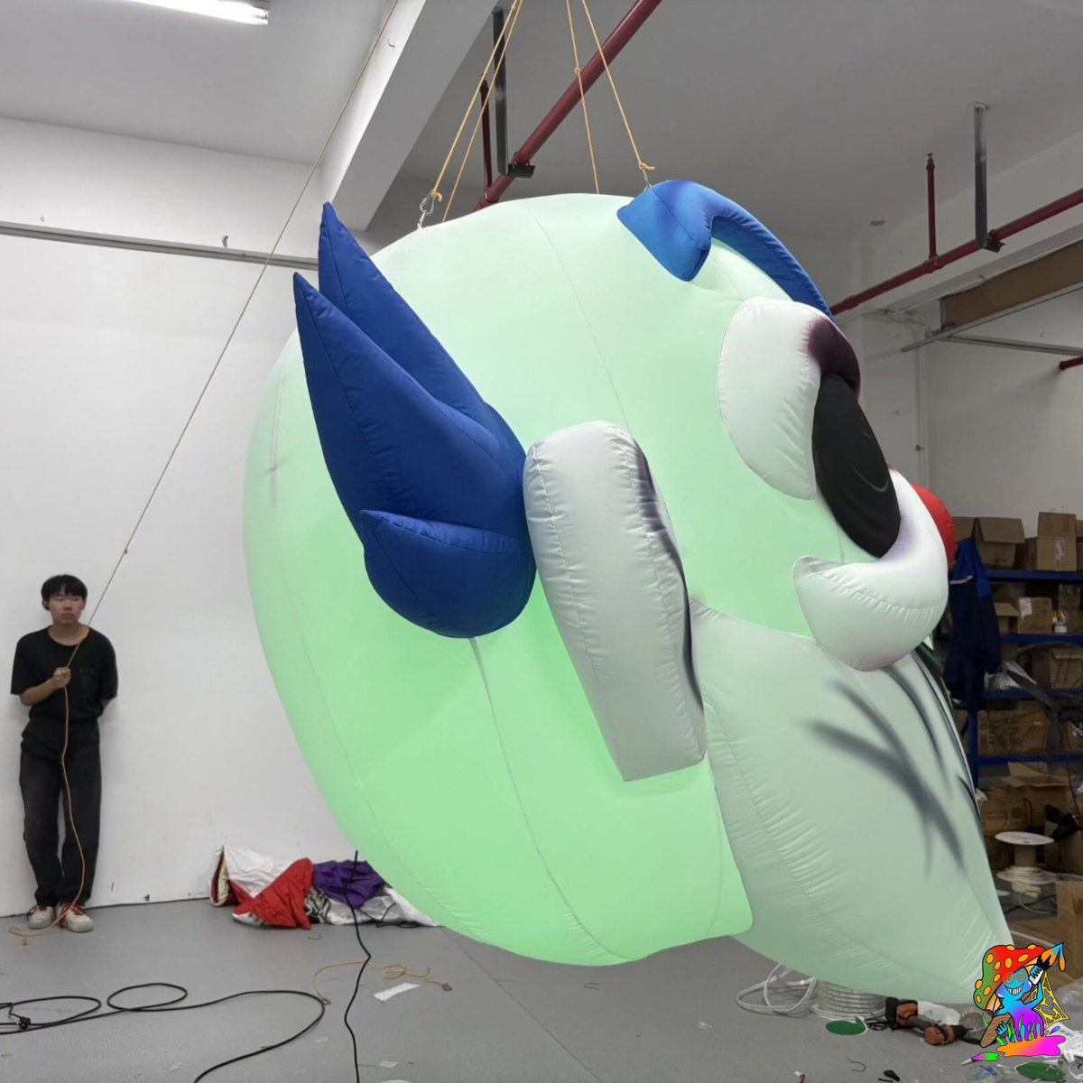 Side and rear view of the green-lit inflatable clown head showing its rounded fabric body and blue hair.