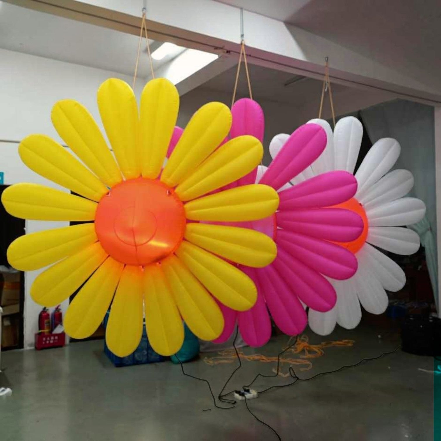 Trippy Creations giant inflatable daisy flower decorations in yellow, pink, and white with orange centers, ideal for events.
