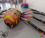 Trippy Creations giant inflatable spider decoration, 5m size, with pink and black legs and a detailed body featuring multiple eyes and yellow accents.