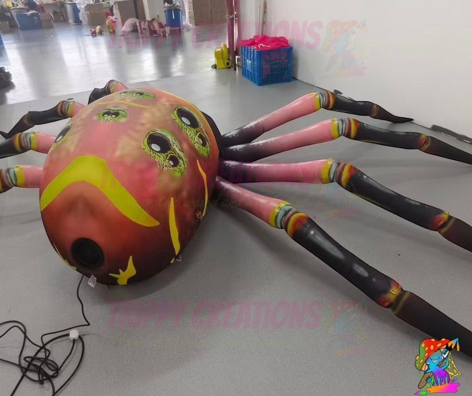 Trippy Creations giant inflatable spider decoration, 5m size, with pink and black legs and a detailed body featuring multiple eyes and yellow accents.