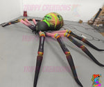 Trippy Creations giant inflatable spider decoration with pink legs and a green and orange body, ideal for Halloween events.