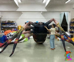 Trippy Creations giant inflatable black spider decoration with long legs, featuring a woman adjusting it. Perfect for Halloween events.